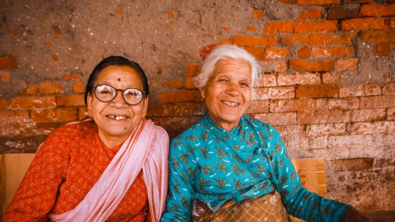 Duas idosas sorriem juntas sentadas lado a lado